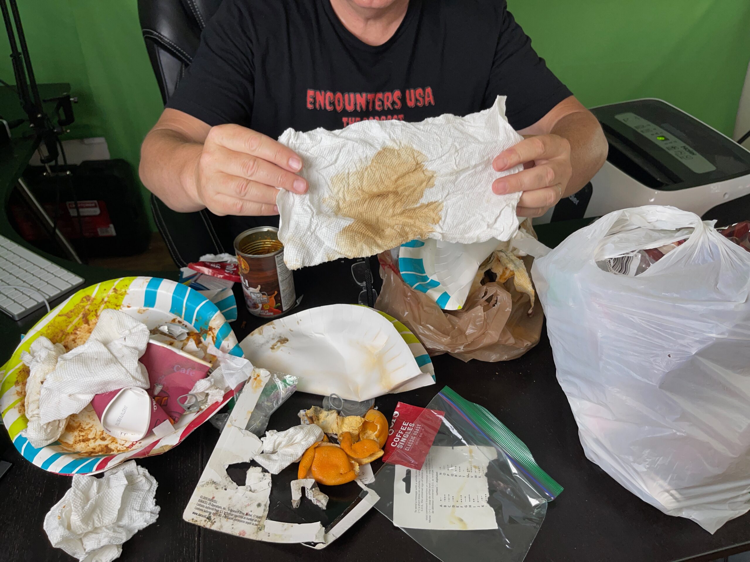 Matthew Heines in Encounters USA shirt holding up a paper towel with a large brownish blood-like stain collected from the center of his tent floor during a field investigation.