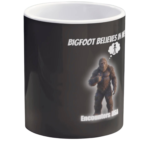 Black ceramic coffee mug with funny Bigfoot design saying "BIGFOOT BELIEVES IN ME" and a thumbs-up Sasquatch with thought bubble. Encounters USA merch.