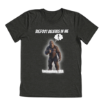 Dark gray tri-blend t-shirt with "BIGFOOT BELIEVES IN ME" and glowing Sasquatch thumbs up design. Funny motivational cryptid tee by Encounters USA.
