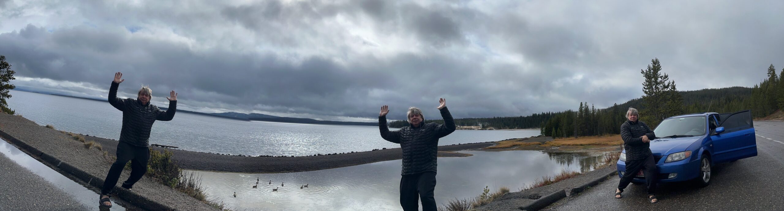 Matthew Heines waving with arms open at a stunning mountain lake in Yellowstone National Park under dramatic cloudy skies