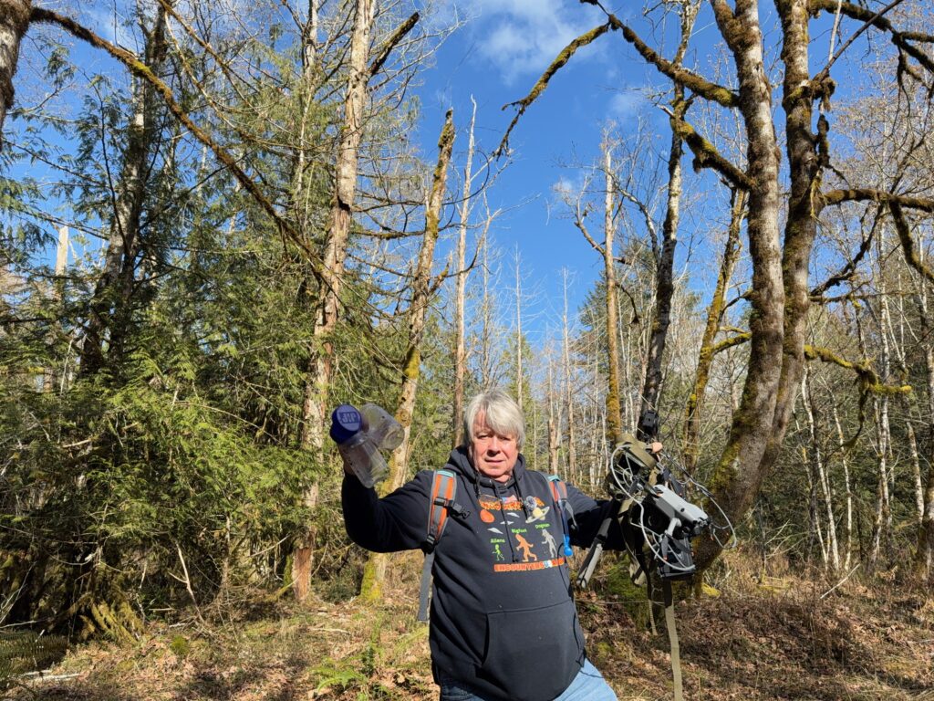 Matthew Heines standing in a Pacific Northwest forest holding a drone and water bottle during field research