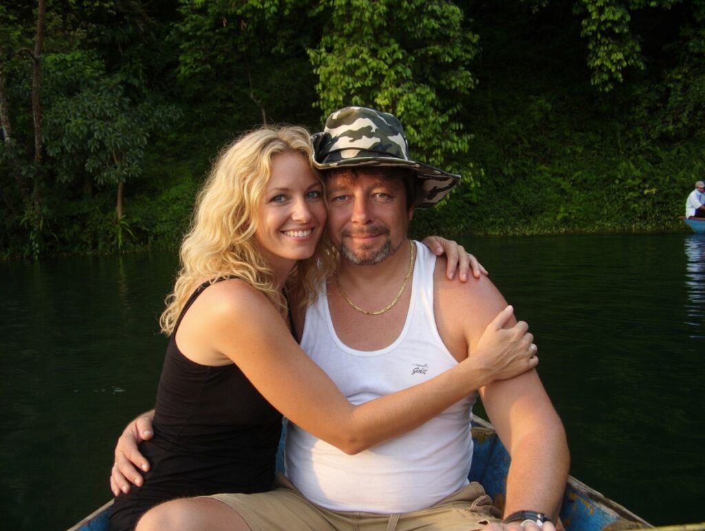 Matthew Heines and Valerie Grok embracing in a boat on a jungle river, smiling together during a romantic getaway