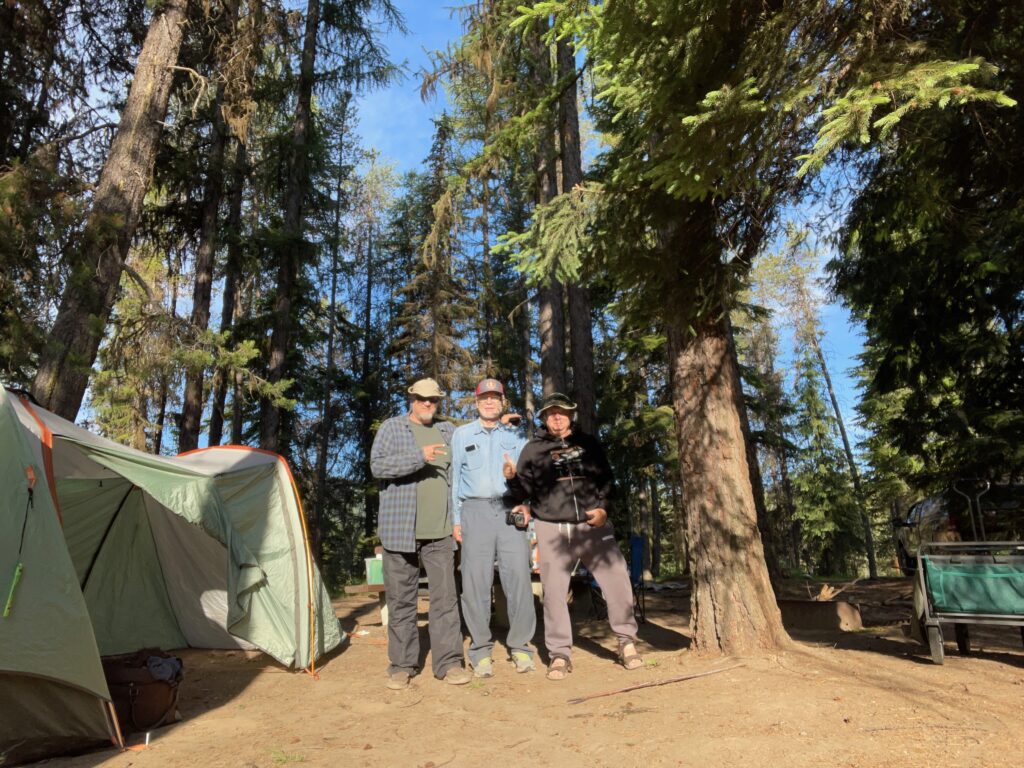 Matthew D. Heines standing with two fellow investigators at a forested campsite in the Northern Cascade Mountains, next to their tent during the Cascade Bigfoot Blood Mystery expedition.