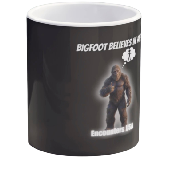 Black ceramic coffee mug with funny Bigfoot design saying "BIGFOOT BELIEVES IN ME" and a thumbs-up Sasquatch with thought bubble. Encounters USA merch.